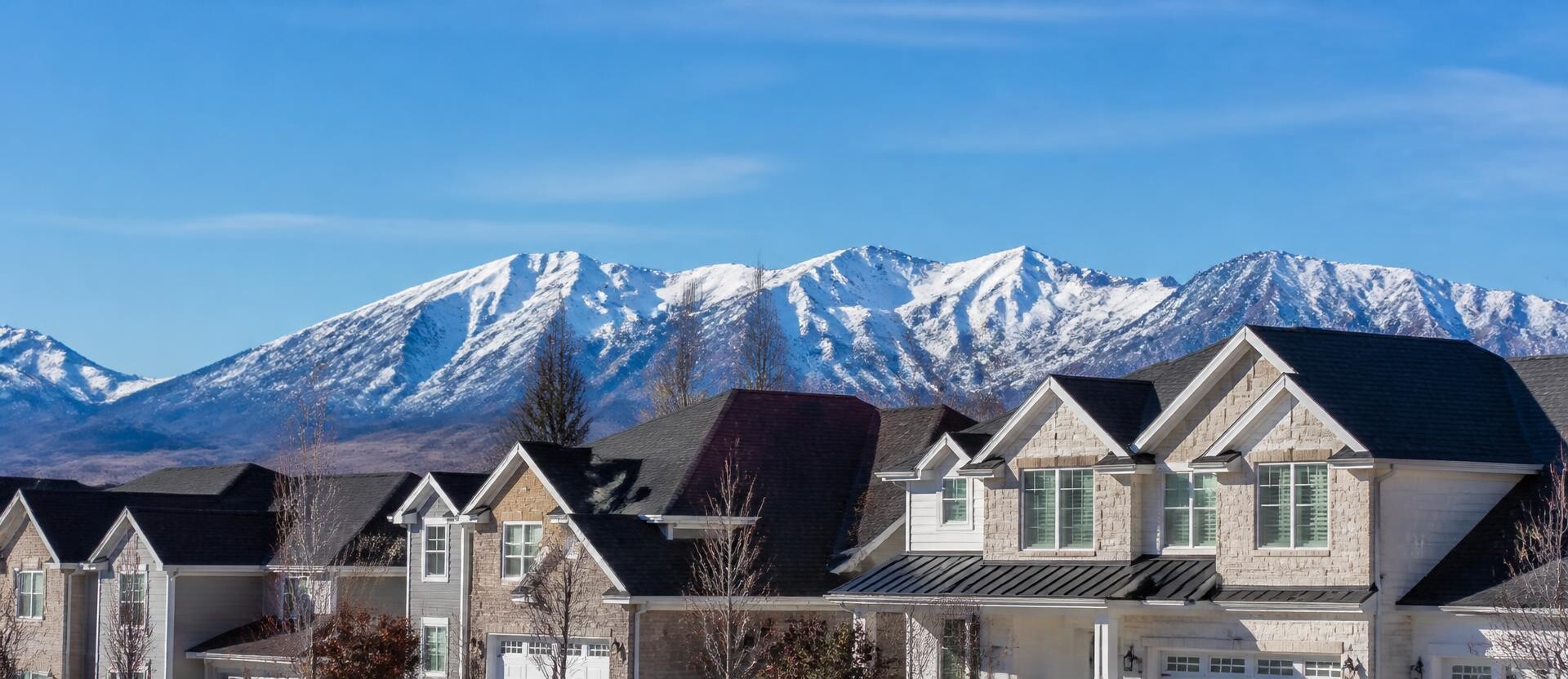 Daytime view of Utah homes with dark shingle roofs and snow-capped mountains in the background