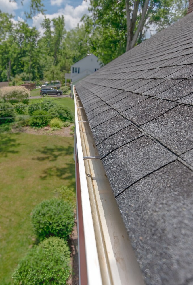 Gutter run along a shingle roof edge with yard in the background