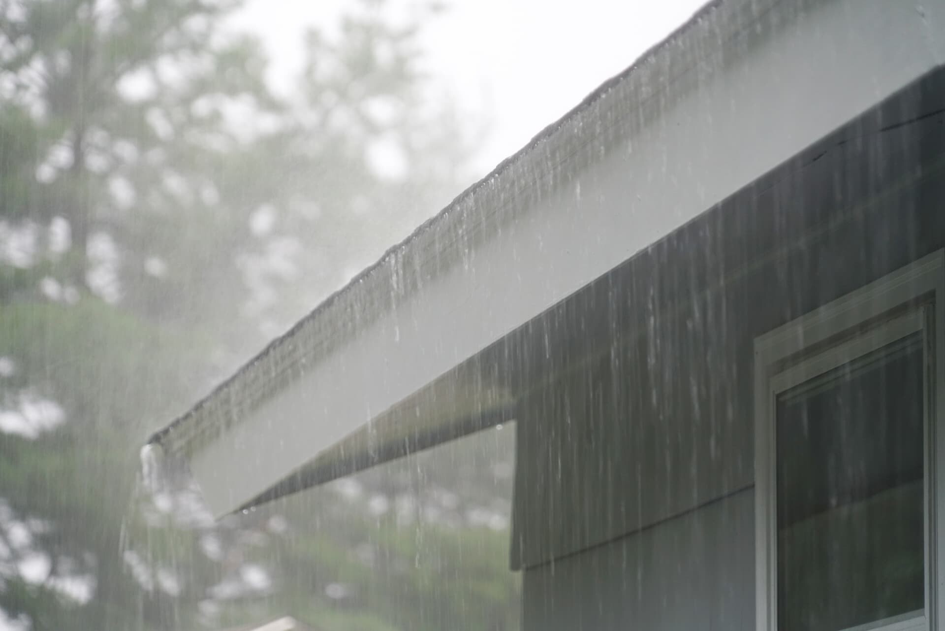 Roof edge without gutters during rain, showing water cascading off the roof