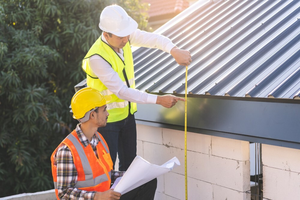 Two roofing contractors measuring a metal roof edge with a tape measure and plans