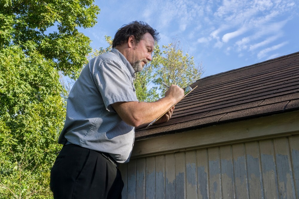 Roofing inspector writing notes on a clipboard while examining a residential roof