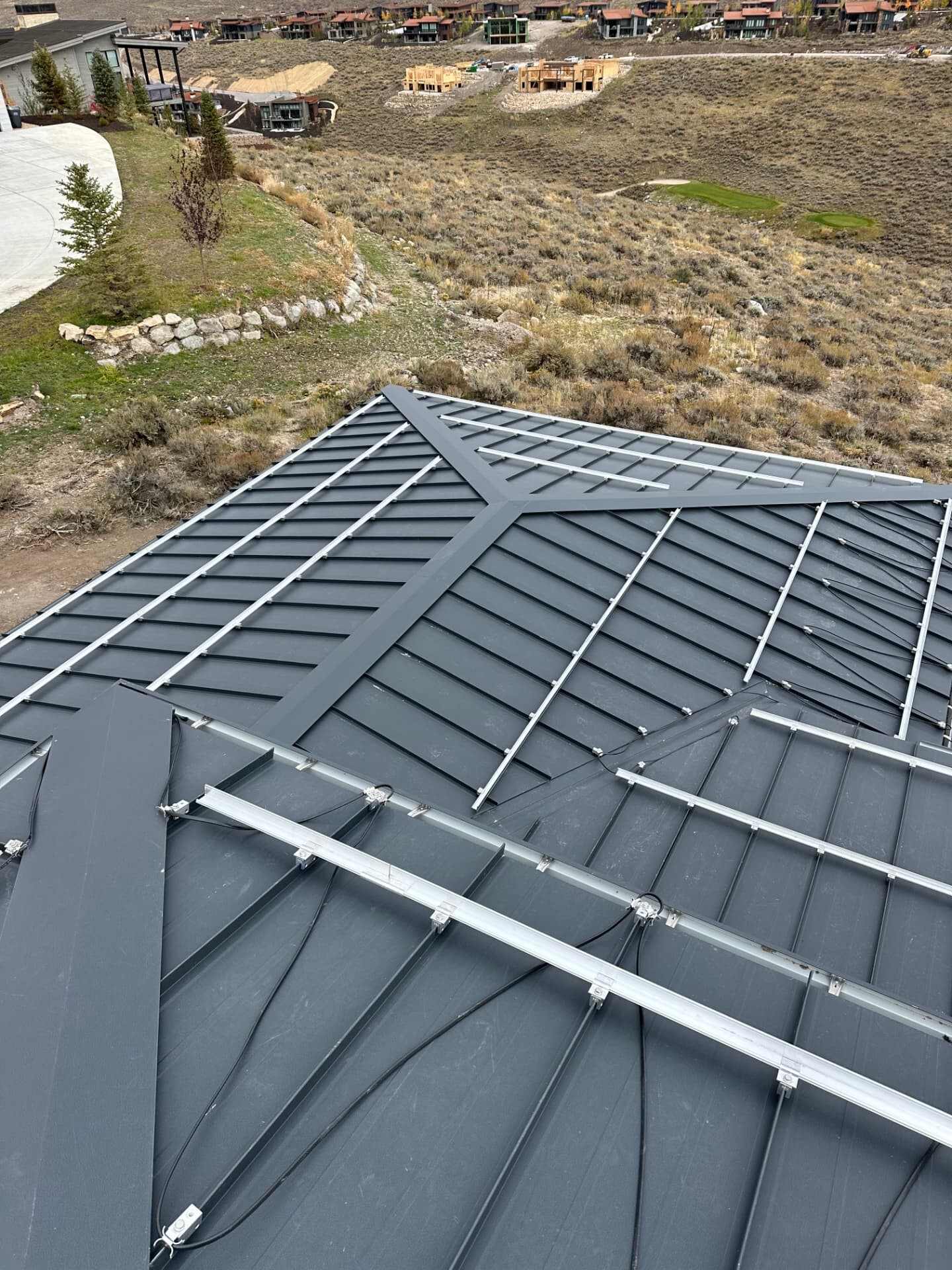 Installed snow retention rails on a dark standing seam metal roof in a Utah hillside community