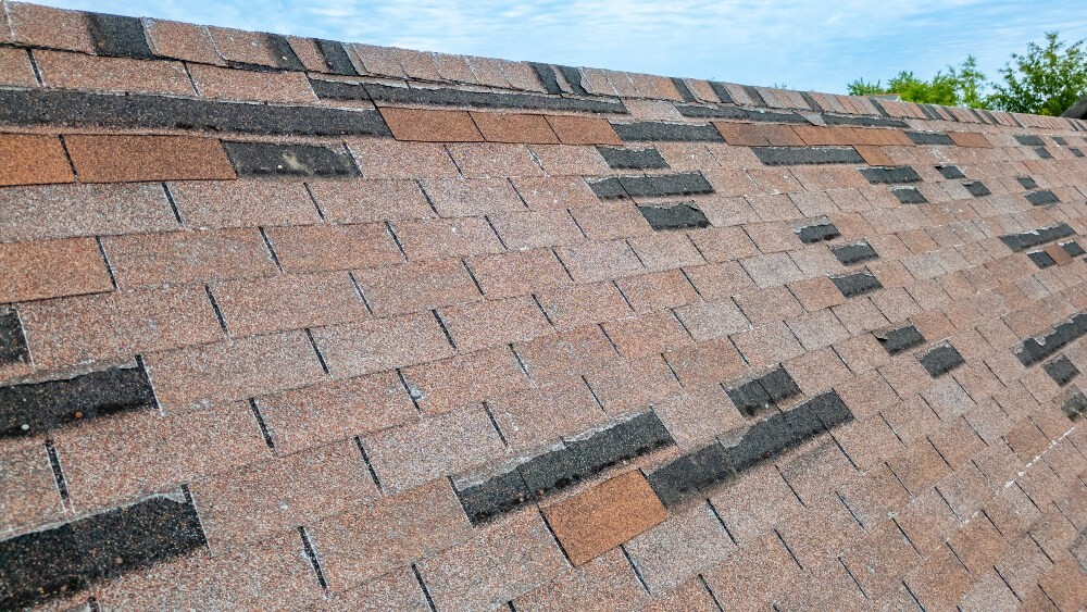 Close-up of a damaged asphalt shingle roof with missing and broken shingles