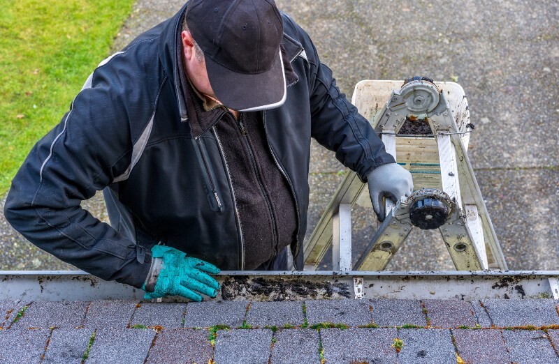 Roofing inspector examining a shingle roof edge from a ladder