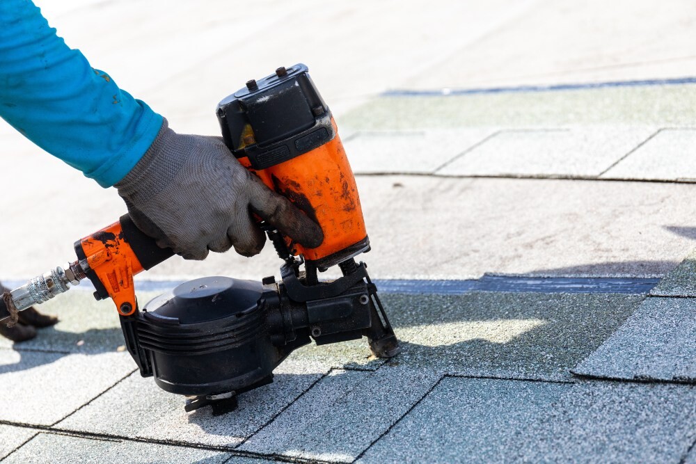 Roofing crew member installing asphalt shingles with a nail gun
