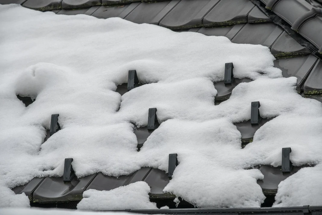 Snow guards on a dark tile roof holding accumulated snow in place