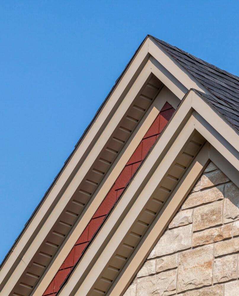 Close-up of a roof edge showing soffit, fascia, and shingles against a clear blue sky
