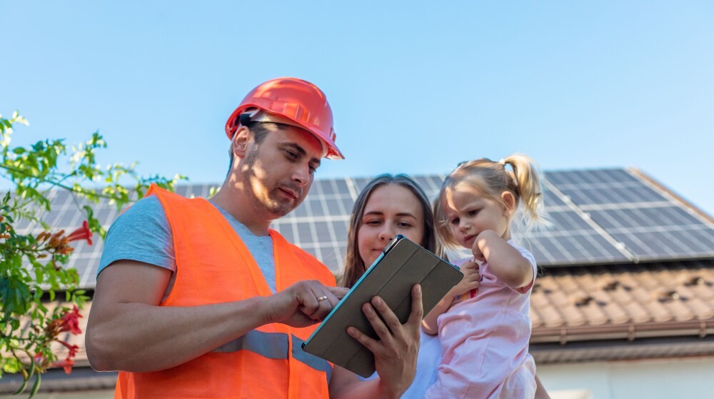 Roofing contractor explaining inspection findings to a homeowner with a child while reviewing a tablet